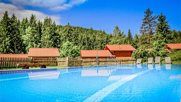 Schönes Schwimmbecken mit Sonnenliegen mit aussiecht auf die mit Tannen bewachsenen Berge und Unsere Ferienhäuser im Camping langenwald